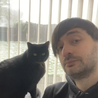 Luke Bickley, with a black cat sitting on the windowsill beside him
